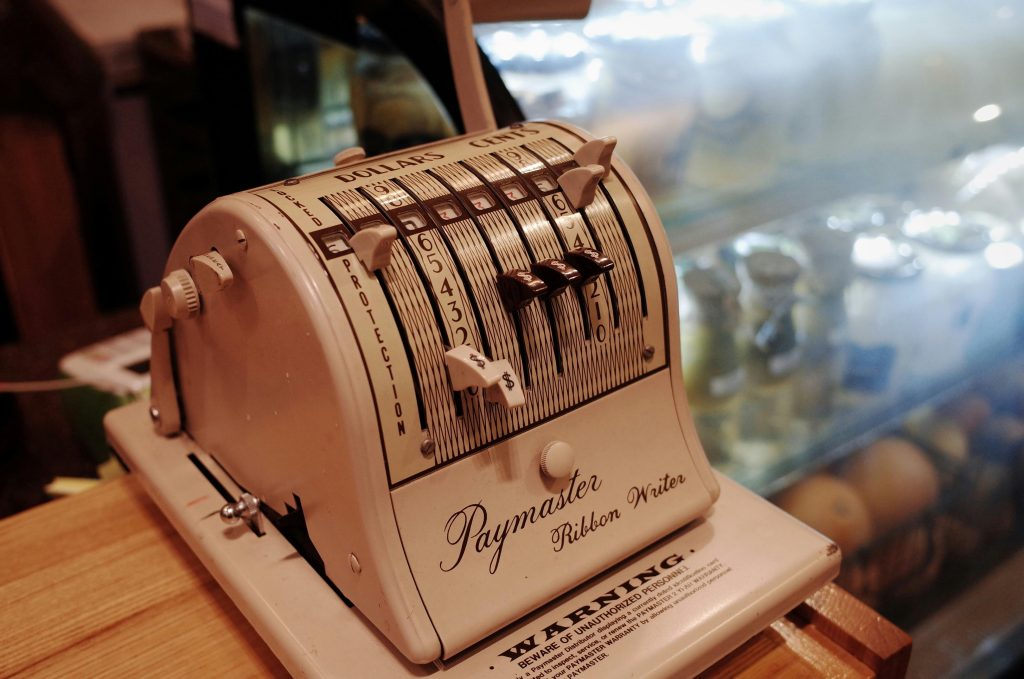 Close-up of a vintage Paymaster Ribbon Writer on a wooden counter in a retro cafe setting.